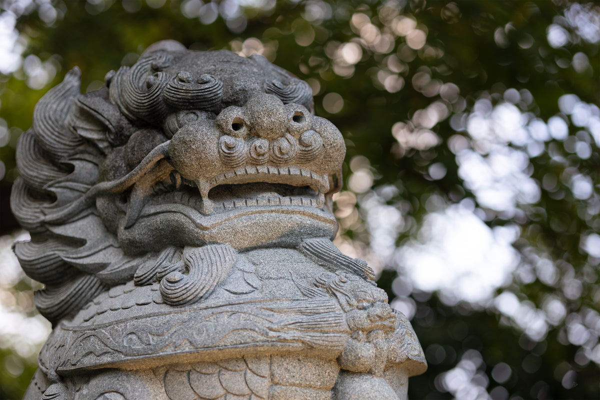 Carved stone guardian lion facing forward, lit from below against sparkling green bokeh.
